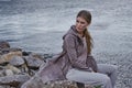 Beautiful sexy young blond woman with long hair and soft natural makeup wearing jacket designer suit sitting in rock stone beach Royalty Free Stock Photo