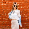 Beautiful sexy young hipster woman in a white lace blouse and denim jacket in black sunglasses in a beige skirt poses near a red Royalty Free Stock Photo