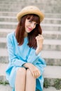 Beautiful sexy young red haired woman wearing blue dress and hat, posing to camera while sitting on city stairs outdoors Royalty Free Stock Photo