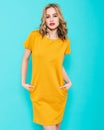 Beautiful young woman in bright yellow party dress studio portrait on pastel blue background. Attractive young woman portrait Royalty Free Stock Photo