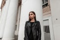 Beautiful sexy young woman in fashionable black clothes posing in the city near a white building with vintage columns. Attractive Royalty Free Stock Photo