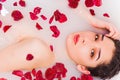 Beautiful young woman having bath with flower petals and looking at the camera, close up Royalty Free Stock Photo