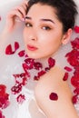 Beautiful young woman having bath with flower petals and looking at the camera, close up Royalty Free Stock Photo