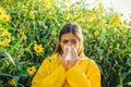 Beautiful young woman lies on flowers background. Young girl sneezing and holding paper tissue in one hand and