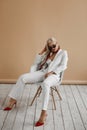 Beautiful young woman with perfect blond hair in elegant white suit and red shoes posing in studio. Fashionable blonde Royalty Free Stock Photo