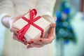 Beautiful young woman in white sweater sitting next to white christmas tree, holding present. Christmas photo.