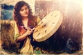 Beautiful shamanic girl playing on shaman frame drum in the nature, old photo effect. Royalty Free Stock Photo