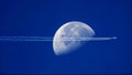 Beautiful shot of an airplane flying and leaving a trail in a blue sky over the moon Royalty Free Stock Photo