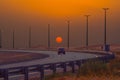 Beautiful shot of a car on the road, sun and street lights during an orange sunset Royalty Free Stock Photo