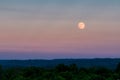 Beautiful shot of the large gray moon in the evening sky over a thick green forest Royalty Free Stock Photo