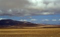 Beautiful shot of an open dry field with mountains and a cloudy blue sky in the background Royalty Free Stock Photo