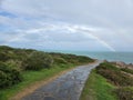 Beautiful shot of a pathway in the beach with a rainbow in the cloudy sky