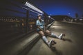 Beautiful shot of short-haired female with roller skates sitting on the curb at night under a light