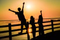 Beautiful shot of silhouettes of happy teenagers on a pier at sunset