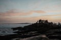 Beautiful shot of silhouettes of people on rocks watching surfers on waves Royalty Free Stock Photo