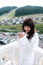 Beautiful shy girl in white hotel bathrobe drinking hot coffee on a balcony. Nature and nice view outside. Quiet weekend getaway