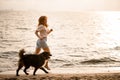 beautiful side view on woman running along sandy beach at water with her dog Royalty Free Stock Photo