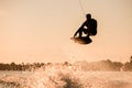 Beautiful silhouette of male rider holding rope and making extreme jump on wakeboard over splashing water. Royalty Free Stock Photo