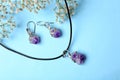 Beautiful silver necklace and pair of earrings with amethyst gemstones on blue background