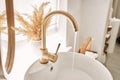 Close-up of an elegant golden faucet in the bathroom sink next to stylish decorations. A beautiful sink with a golden Royalty Free Stock Photo