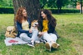 Beautiful sisters talking stroking dog sitting on lawn in park enjoying summer Royalty Free Stock Photo