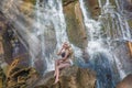 Beautiful skinny girl posing on the background of a waterfall splashing water and bright sun.