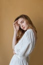 Beautiful skinny young girl with long hair in white dress on beige background with cute smile looking at the camera