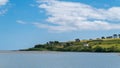 Beautiful sky over a calm water surface on a summer day. The picturesque green coast of Ireland. Several buildings on the hill.