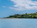 Beautiful sky over a water on a summer day. The picturesque green coast of Ireland. Several buildings on the hill. Seascape. Green