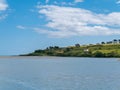 Beautiful sky over a water surface on a summer day. The picturesque green coast of Ireland. Several buildings on the hill.