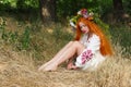 Beautiful slavic girl with long red hair with flower crown in embroidered ethnic suit sitting on lawn. Feast of Ivan Kupala Royalty Free Stock Photo