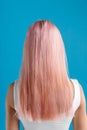 Beautiful sleek natural long pink color dyed hair of young woman standing isolated over blue studio background