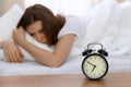 Beautiful sleeping woman lying in bed and trying to wake up with alarm clock. Girl having trouble with getting up early