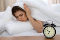 Beautiful sleeping woman lying in bed and trying to wake up with alarm clock. Girl having trouble with getting up early