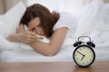 Beautiful sleeping woman lying in bed and trying to wake up with alarm clock. Girl having trouble with getting up early