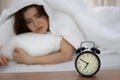 Beautiful sleeping woman lying in bed and trying to wake up with alarm clock. Girl having trouble with getting up early