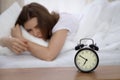 Beautiful sleeping woman lying in bed and trying to wake up with alarm clock. Girl having trouble with getting up early Royalty Free Stock Photo