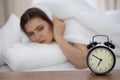 Beautiful sleeping woman lying in bed and trying to wake up with alarm clock. Girl having trouble with getting up early