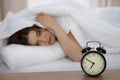 Beautiful sleeping woman lying in bed and trying to wake up with alarm clock. Girl having trouble with getting up early