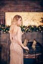 Beautiful slender blonde woman in Golden dress stands with champagne on her hand indoors near the fireplace and Christmas Royalty Free Stock Photo