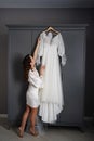bride in a silk robe next to a white wedding dress hanging on the closet.
