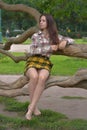 Slender brunette girl in a plaid skirt and blouse in the summer by a tree in the park