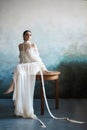 Beautiful slender brunette girl sitting on the sofa in a long white dress. Portrait of a woman with a jewellery on neck. Perfect Royalty Free Stock Photo