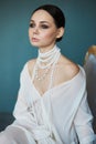 Beautiful slender brunette girl sitting on the sofa in a long white dress. Portrait of a woman with a jewellery on neck. Perfect Royalty Free Stock Photo