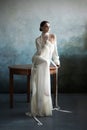 Beautiful slender brunette girl sitting on the sofa in a long white dress. Portrait of a woman with a jewellery on neck. Perfect Royalty Free Stock Photo