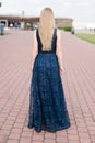 Slender blonde girl in dark-blue floor-length dress turned her back on the pavement Royalty Free Stock Photo