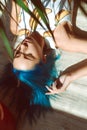 Beautiful slender girl in panties and a T-shirt with blue hair posing on the floor next to a flower in a pot Royalty Free Stock Photo