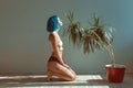 Beautiful slender girl in panties and a T-shirt with blue hair posing on the floor next to a flower in a pot Royalty Free Stock Photo