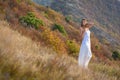 A beautiful slender girl in white clothes stands on the mountainside