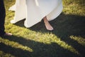 Beautiful slender legs of a bride in a white dress barefoot on a green lawn. Royalty Free Stock Photo